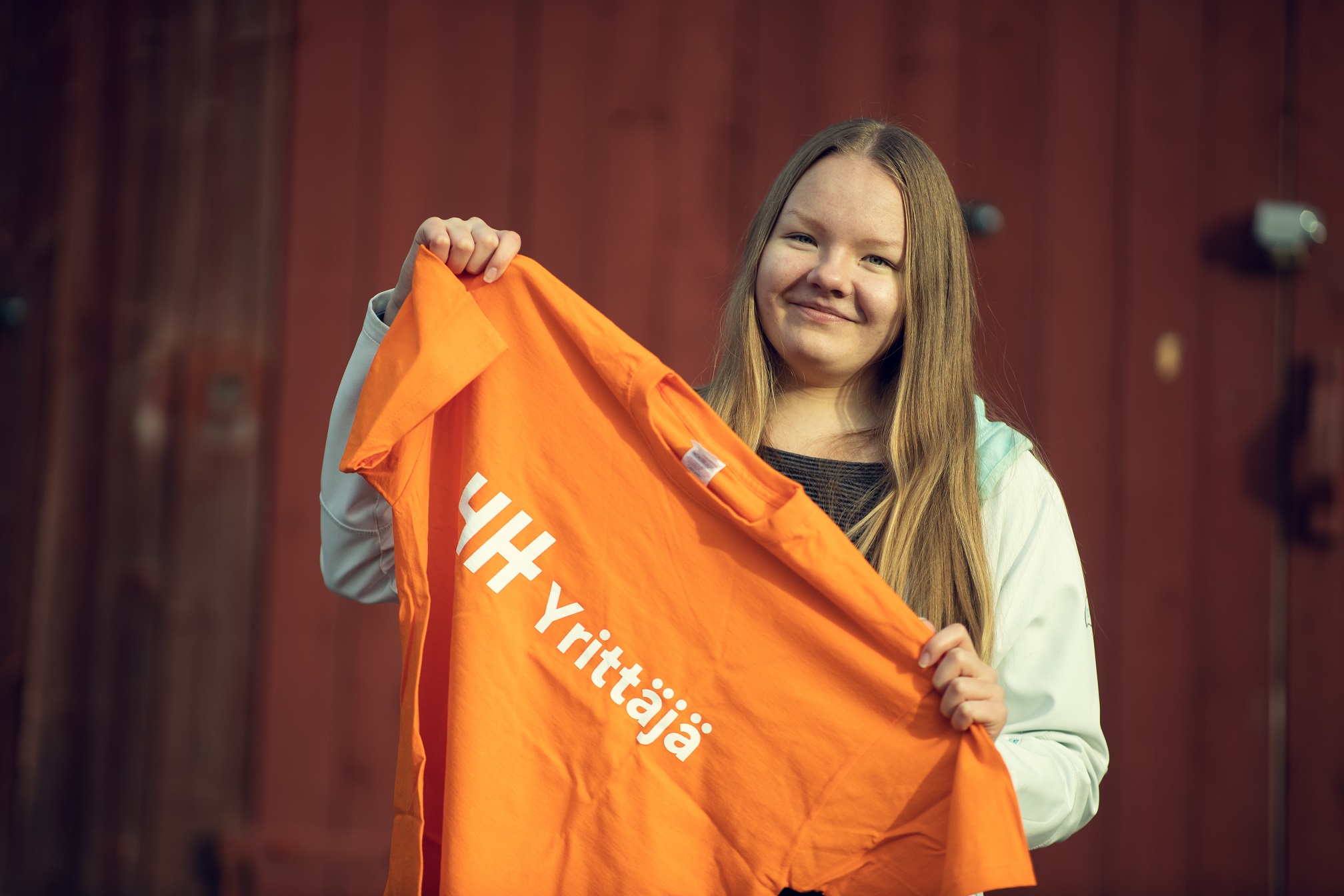 Nuori nainen pitämässä käsissään oranssia 4H yrittäjä t-paitaa.