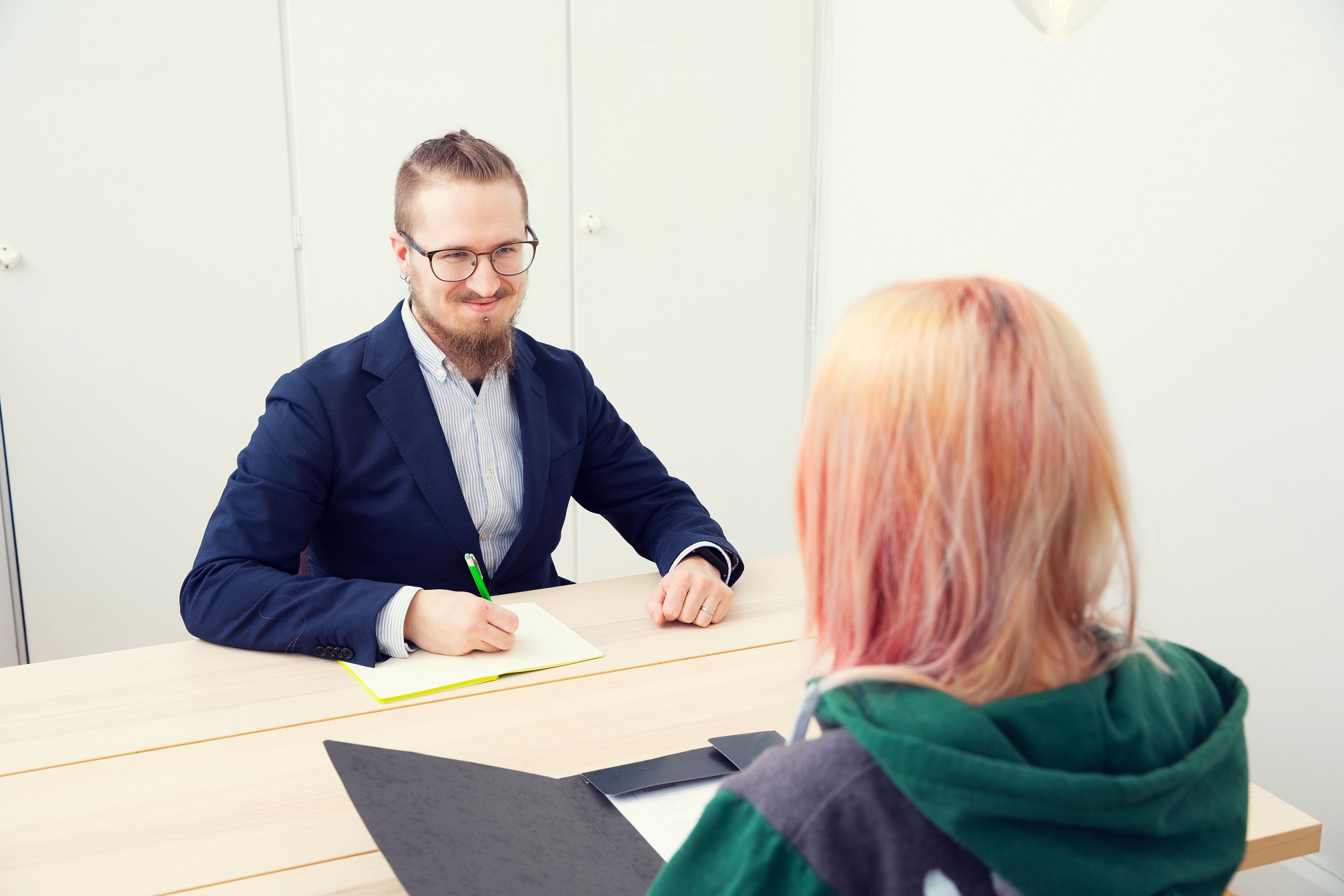 Silmälasipäinen mies pikkutakissa haastattelee punahiuksista nuorta pöydän äärellä.