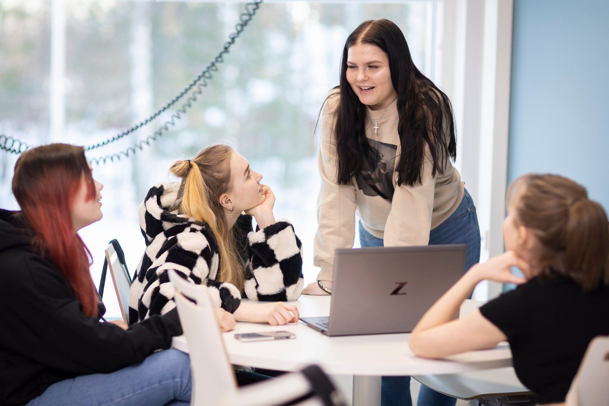 Neljä nuorta juttelemassa pöydän ääressä tietokoneen vieressä.