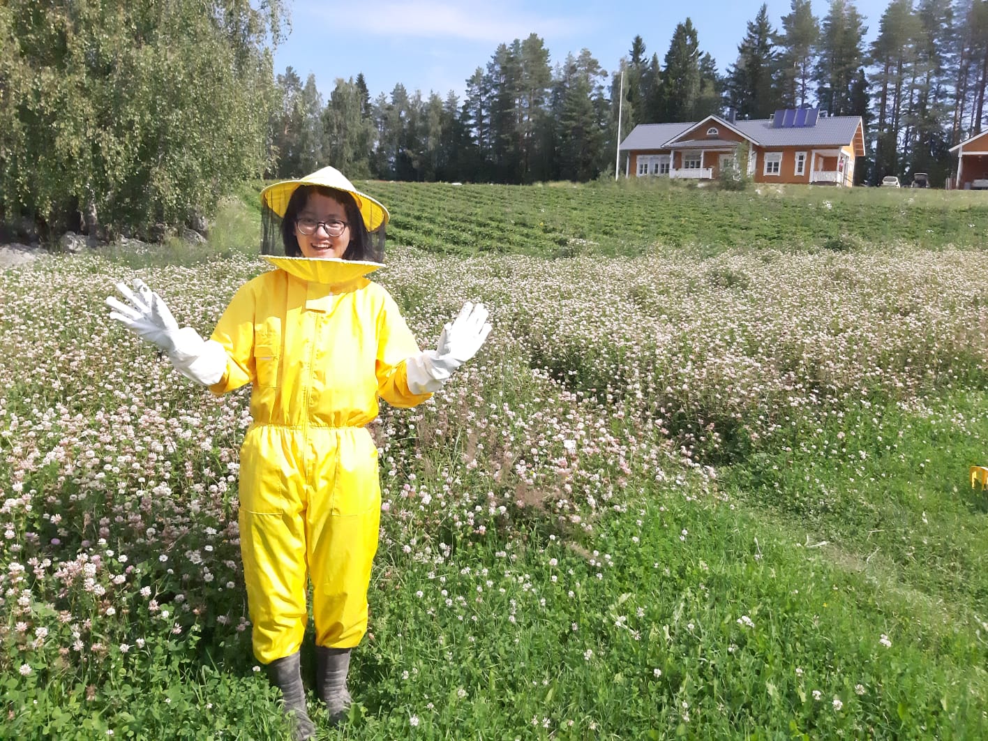 Nuori seisoo kukkakedon edessä päällään keltainen mehiläishoitajan suojahaalari.
