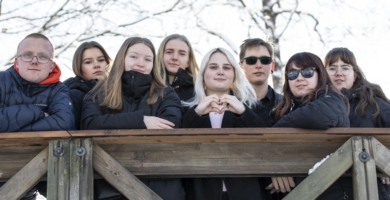 Vaikuttajanuoria seisomassa ulkona kaiteen takana talvitakit päällä.