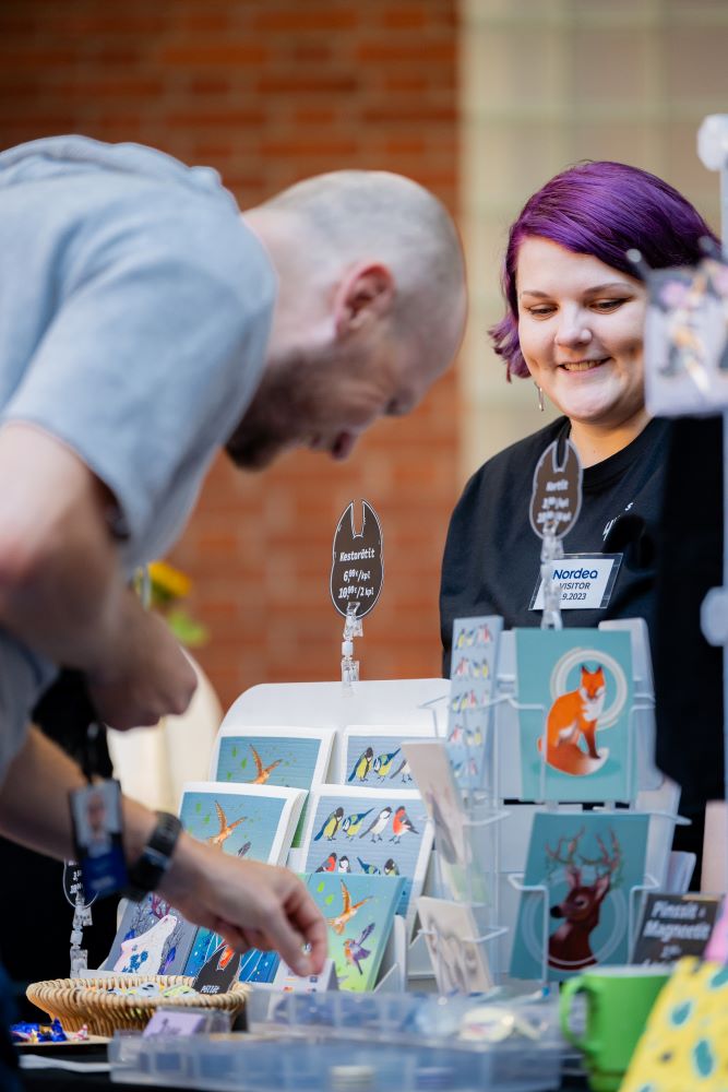 Asiakas tarkastelee myyntipöydällä esillä olevia taidetuotteita.