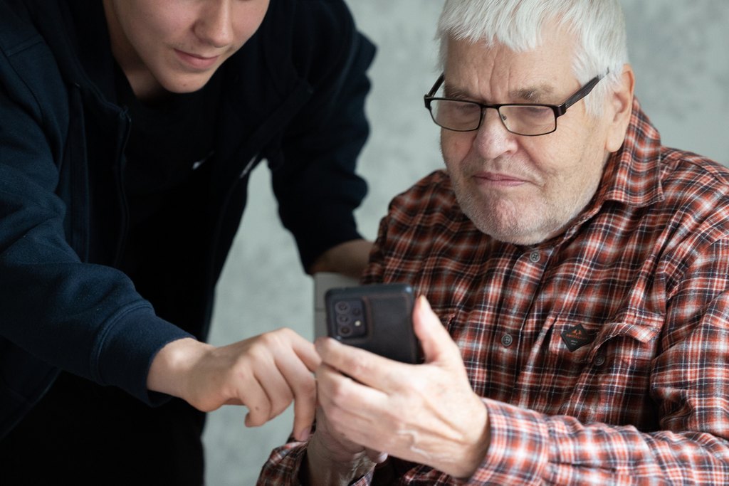 Nuori auttamassa senioria puhelimen kanssa